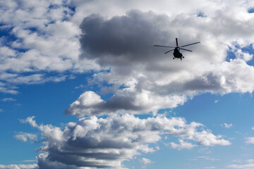 Fototapeta na wymiar Cumulus clouds against the blue sky, silhouette of a flying helicopter