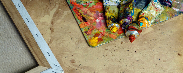 Banner tubes of multicolor oil paint and artist's brushes on canvas close-up.