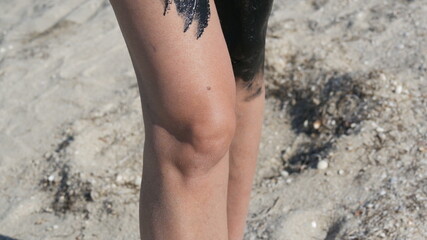 Healing black medical mud applies to leg and knee woman at the lake of salt water. Salty black dirt for people with health and skin problems. Relax at spa resort. Exfoliation scrub beauty treatment.