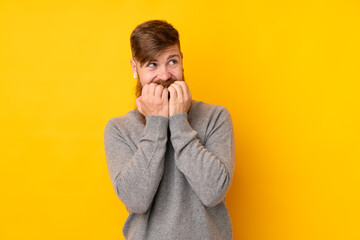 Redhead man with long beard over isolated yellow background nervous and scared putting hands to mouth