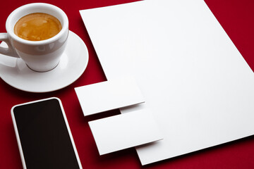 Coffee, devices, blank flyer posters and cards floating above red background. Office styled, modern mockup for advertising, image or text. Blank white copyspace for design, business and finance