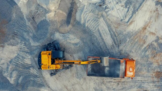 Excavator loading crushed stone into a dump truck in a crushed stone quarry. Aerial top down view 