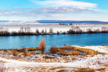 Fototapeta premium Winter landscape with river and snow-covered grass by the river