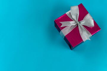 Top view of gift box wrapped in red paper with ribbon on blue colour background. Copy space for text. Holiday concept. Time gifts.