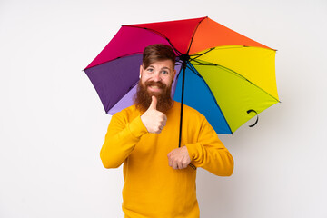Redhead man with long beard holding an umbrella over isolated white background giving a thumbs up...