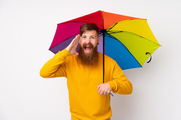 Redhead man with long beard holding an umbrella over isolated white background shouting with mouth...