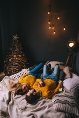 couple in love lie on bed and want to kiss. garlands on the wall and Christmas tree near the bed. White room