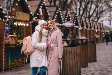 Obraz premium Two young women walking on the decorated street, girls in a winter coat walking on a festive street in the morning.