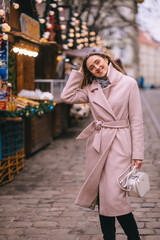 Fototapeta premium Street portrait of smiling beautiful young woman on the festive Christmas fair. Lady wearing classic stylish winter knitted clothes.