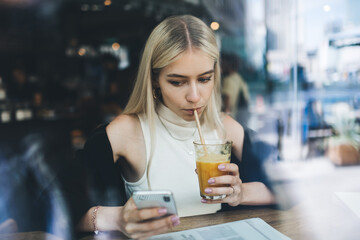 Concentrated woman drinking juice and using smartphone