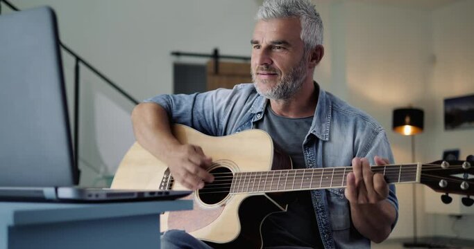 adult mature man learning to play guitar following online tutorialon the computer,active person having fun playing musical instrument,creativity hobby passion