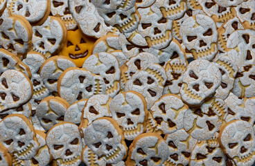 Skull-shaped chocolate cookies all over the image with a single pumpkin cookie. 