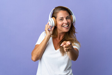 Middle age brazilian woman isolated on purple background listening music and pointing to the front