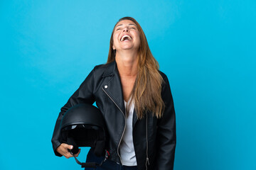 Middle age woman holding a motorcycle helmet isolated on blue background laughing