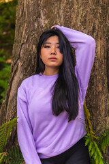 Portrait of a young Asian brunette in a park next to a tree with a pink sweater. Lifestyle, portrait Asian girl