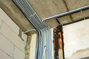 Electrical cables laid in protective corrugation installed on the ceiling and wall in a room under construction works.