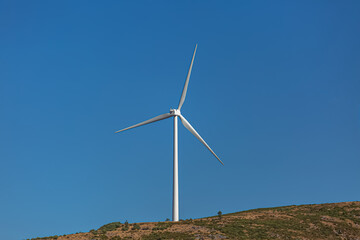 View of a wind turbine on top of mountains, blue sky as background in Portugal