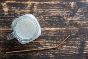 Glass jar of banana milkshake on wooden background. Top view, copy space