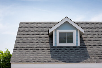 Roof shingles with garret house on top of the house among a lot of trees. dark asphalt tiles on the...