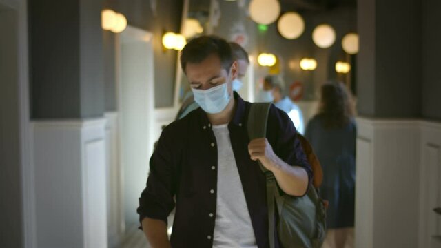 Portrait of guy with backpack wearing safety mask walking in college corridor