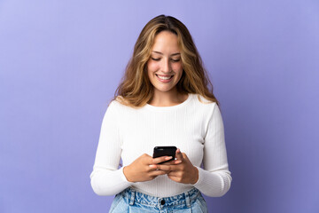 Naklejka premium Young blonde woman isolated on purple background sending a message or email with the mobile