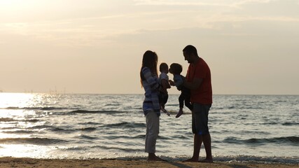 Funny brother kissing baby child, parent silhouettes holding children at seaside, tender and pure love, family summer lifestyle