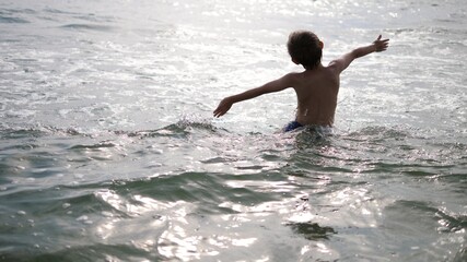 child with hands up goes into the sea