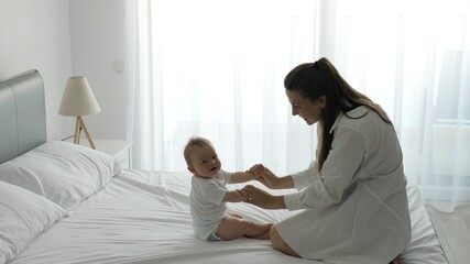 Obraz premium Mother holding baby hands lift up child from bed, healthy exercises