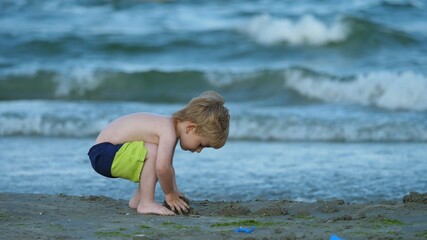 Active blond hair child play with sand at seashore, blue waving ocean