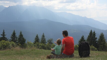 Father and son sit and look at mountains top, holiday in nature, sun rays shine