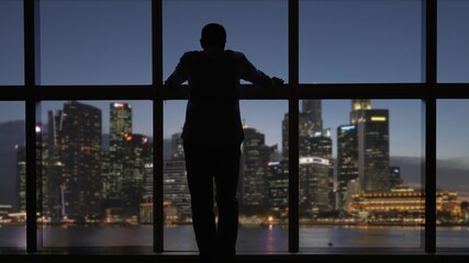 Fototapeta na wymiar Businessman end of day at office, look through window at city dusk