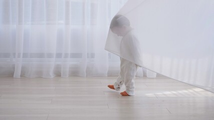 Funny little child playing behind the curtain at home