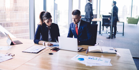 Caucasian business persons in formal clothing sitting at table desktop with modern technology for digital marketing and discussing exchange documents during brainstorming collaboration in office