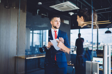 Successful male and female proud ceo discussing business strategy for financial project analyzing paper report in office workspace, formally dressed colleagues talking about exchange productivity