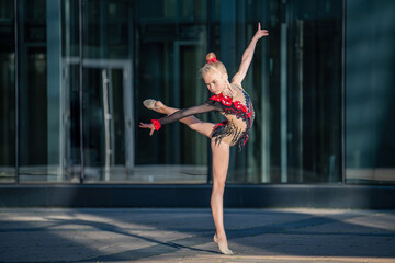 A girl gymnast of school age in a beautiful cross-dress with a black suit performs an exercise without an apparatus.