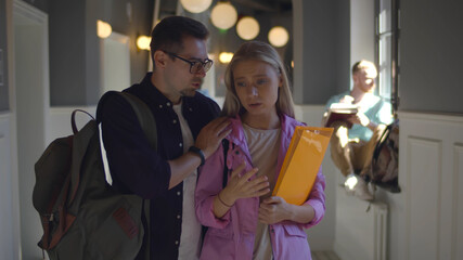 Guy friend comforting sad female student with failed exam walking in college corridor