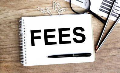 FEES. text on white paper on a wooden background, near financial charts, calculator, magnifying glass