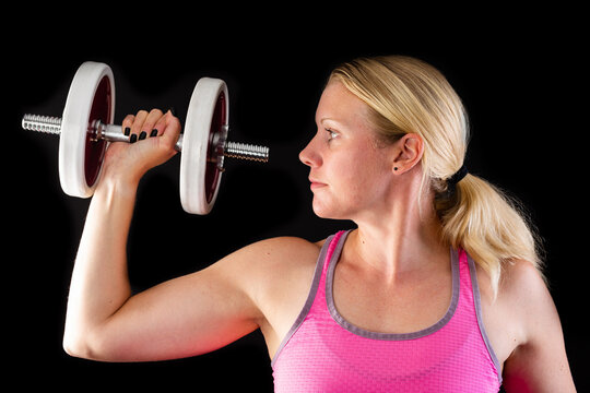 Fitness woman wearing pink top lifting dumbbell isolated on black background