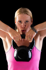 Fitness woman wearing pink top lifting kettlebell isolated on black background