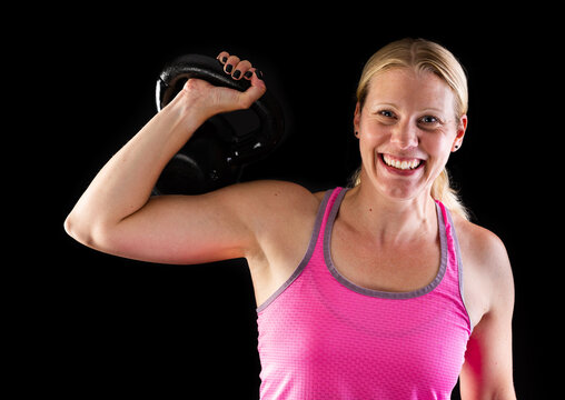 Fitness woman wearing pink top lifting kettlebell isolated on black background