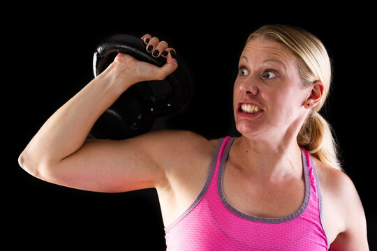 Fitness woman wearing pink top lifting kettlebell isolated on black background
