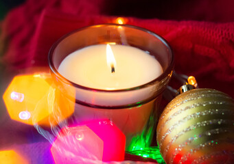 candle with lights and a Christmas ball on a red cozy knitted sweater. selective focus