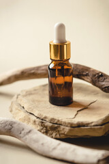 One brown bottle of cosmetics on a natural beige background. A stone podium and a driftwood. Front...