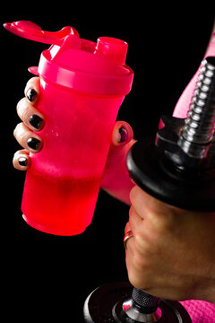 Woman holding energy drink in pink bottle while lifting dumbbell