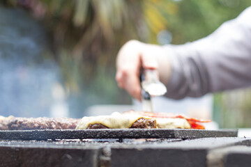 Cooking beef burgers with cheese on top on a grill outdoors in a pub in London, Uk.