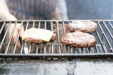 Cooking beef burgers with cheese on top on a grill outdoors in a pub in London, Uk.
