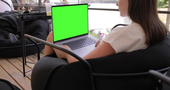 Woman watching on MacBook Pro with keyed blank green screen in outdoor cafe food market. Travel freelance business lifestyle. Internet communication chat. Typing message, searching. Chromakey mockup