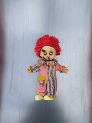 scary toy clown with red hair and closed eyes lies on a new metal background