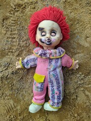 scary toy clown with red hair and closed eyes lying on the sand