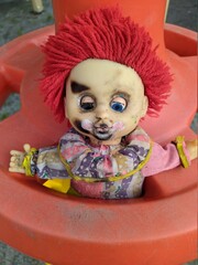 scary toy clown with red hair and half open blue eyes and outstretched hands in a plastic wheel
